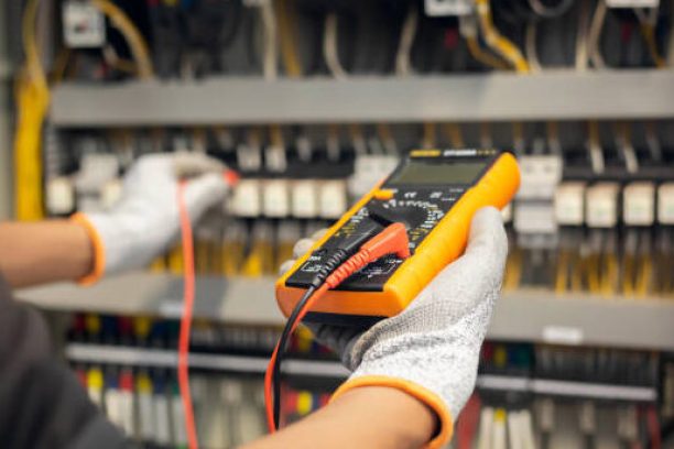 Electrician engineer uses a multimeter to test the electrical installation and power line current in an electrical system control cabinet.